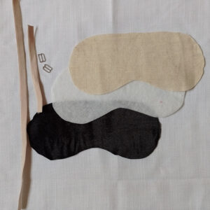 Beige bra elastic, two silver sliders. Blak velvet, fusible batting and beige linen cut out in the shape of a sleep mask template.
