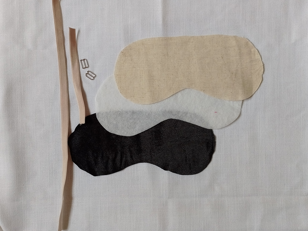 Beige bra elastic, two silver sliders. Blak velvet, fusible batting and beige linen cut out in the shape of a sleep mask template.