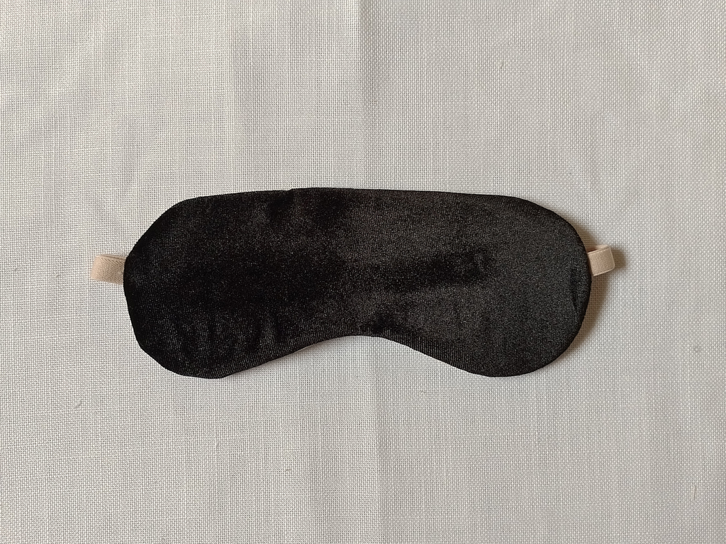 The front of a sleep mask. It has black velvet fabric and a beige adjustable strap
