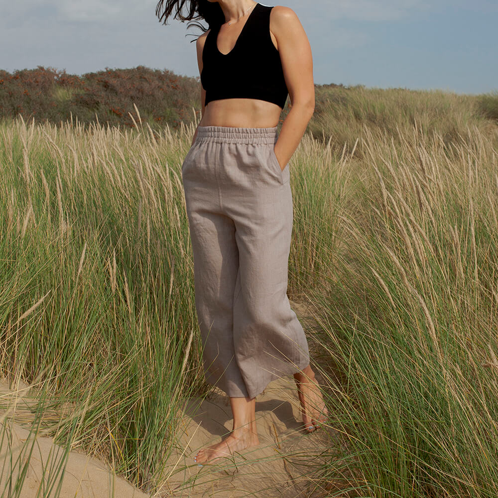 Woman wearing light grey wide leg culottes with elastic waistband, standing barefoot in a grassy outdoor setting.