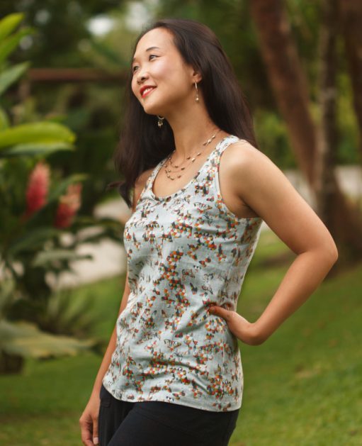 Woman wearing a sleeveless floral tank top, standing outdoors with one hand on her hip.