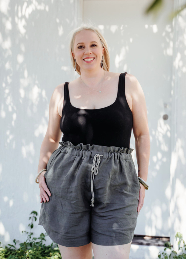 Woman wearing a black tank top and olive green drawstring paperbag waist shorts, standing outdoors.