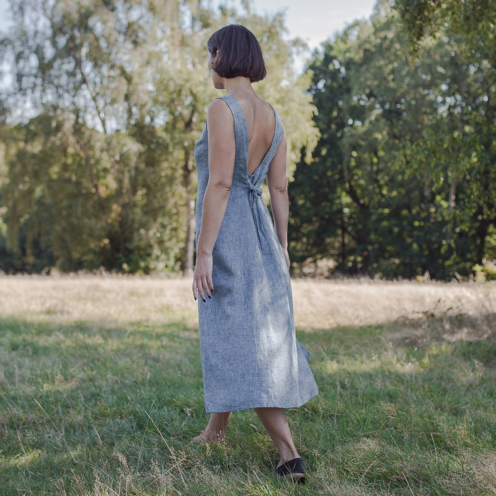 Woman wearing a backless blue maxi dress with tie detail, standing outdoors on grass.