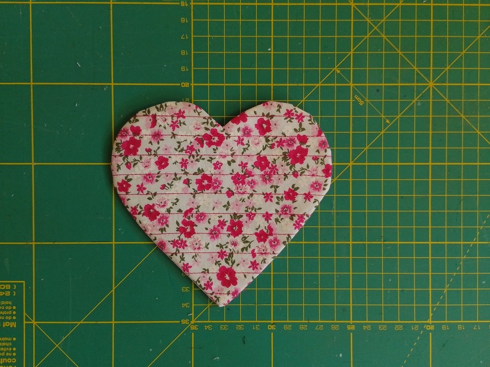 A heart shaped fabric coaster on a green cutting mat.