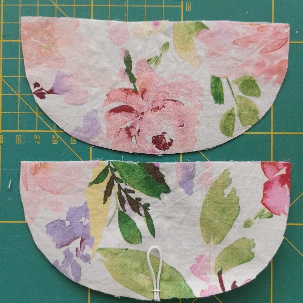 Two flap fabric pieces with one flipped right side down and pinned with a folded elastic loop at the center bottom edge.