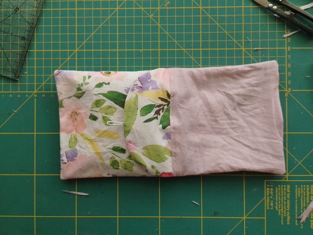 Sewn pouch body laid flat, showing floral outer fabric with flap and plain pink lining fabric.