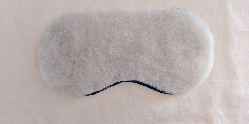The white, fluffy batting piece cut in the shape of an eye mask, placed on top of a matching piece of dark teal fabric.