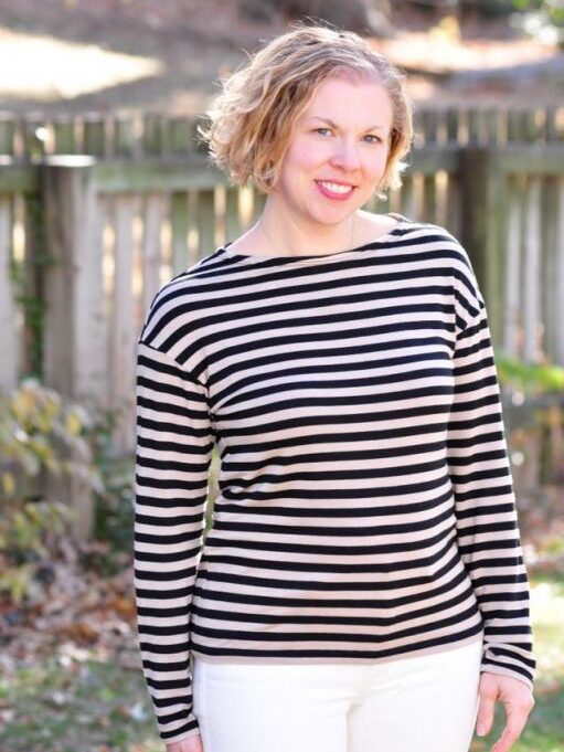 A woman with short blonde hair smiles while wearing a long-sleeved, black and white striped t-shirt outdoors.