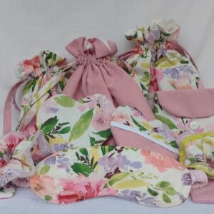 A collection of handmade sewing projects are displayed together in a group shot. The items, all made from matching floral and solid pink fabrics, include drawstring bags, a sleep mask, heart-shaped coasters, scrunchies, and a small pouch.