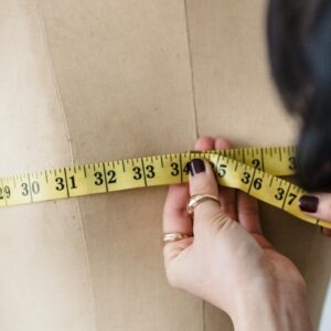 A woman's hands measuring the bust of a dress form with a yellow tape measure.