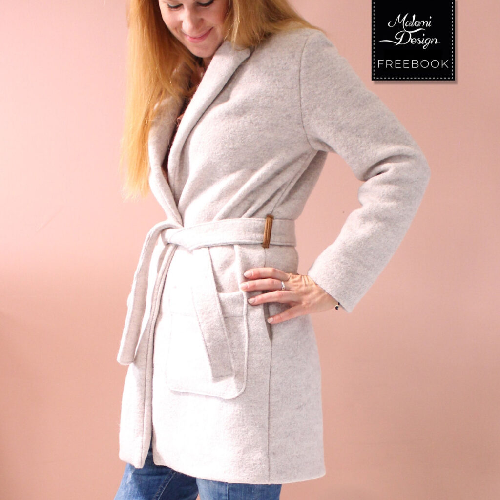 A woman wearing a light beige, knee-length wrap coat with a tie belt and large patch pockets.