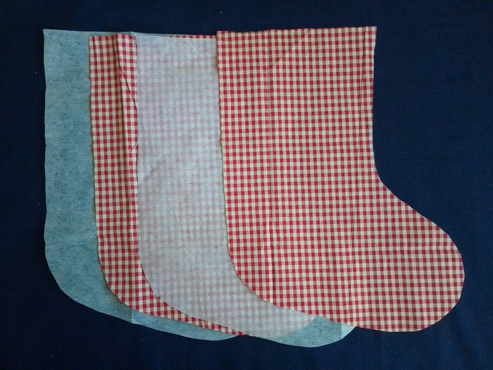 Four stocking-shaped fabric pieces fanned out on a dark blue background. From left to right: white interfacing, red and white gingham, white interfacing, red and white gingham