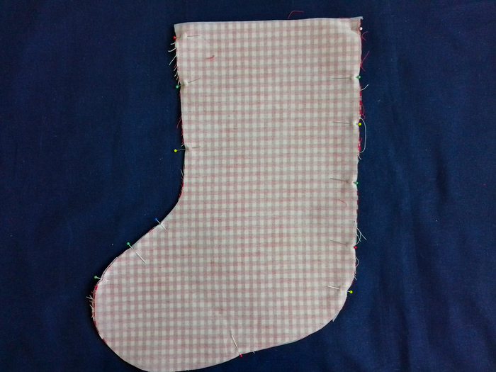 Two stocking-shaped pieces of red and white gingham fabric pinned together, with the wrong side of the fabric facing up.