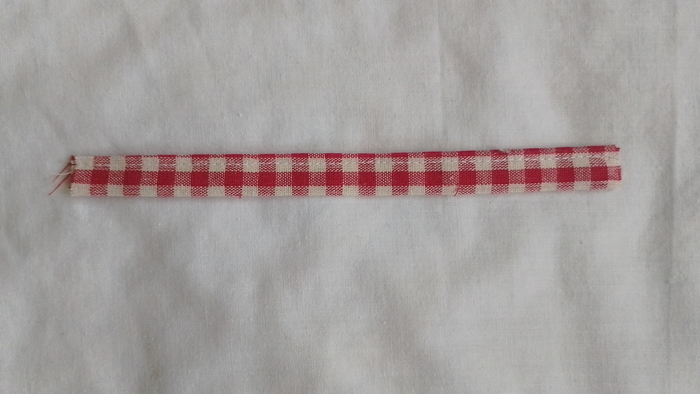 A finished, topstitched strap made of red and white gingham fabric lying horizontally on a white background.