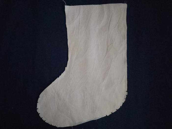 An off-white calico christmas stocking lining with the seam allowance along its curved edges clipped into small notches.