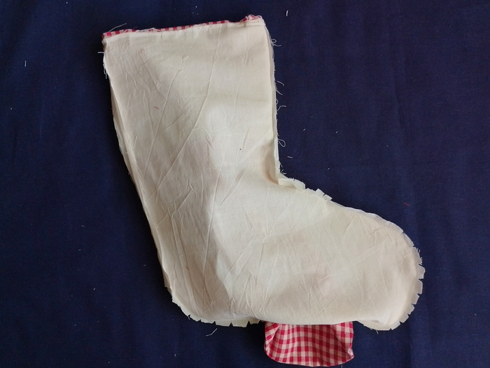 A red and white gingham stocking partially pulled through the open bottom seam of an off-white calico lining.