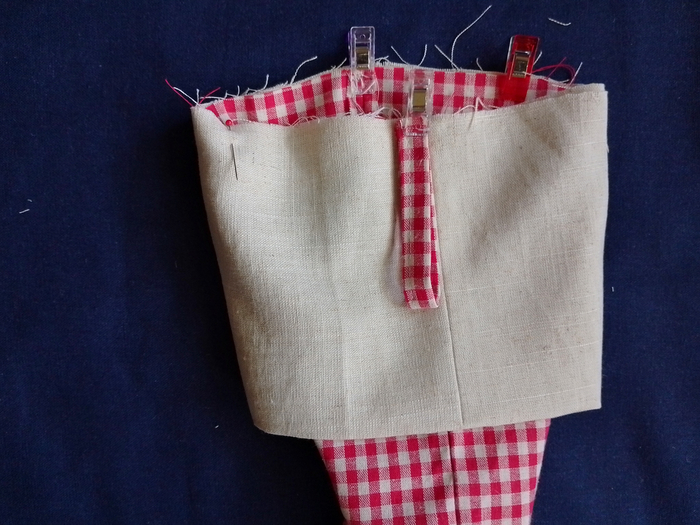 A close-up of a stocking's top edge, showing a gingham hanging loop on top of the off white linen cuff that is attached to the main stocking.