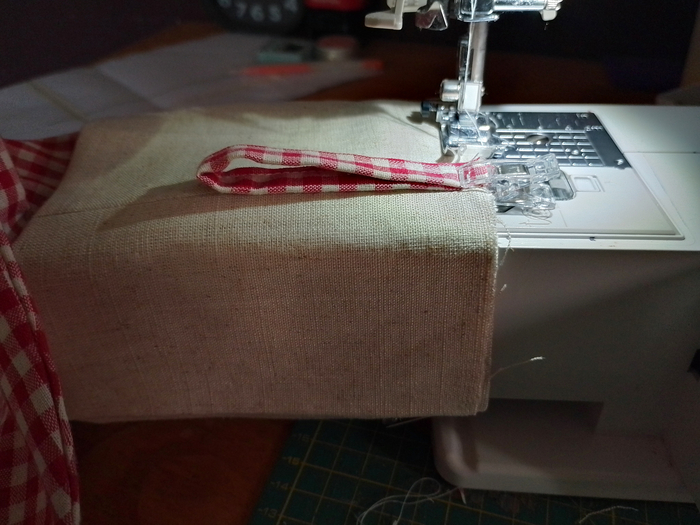 The top edge of the stocking, with the cuff and hanging loop in place, positioned under the presser foot of a sewing machine.