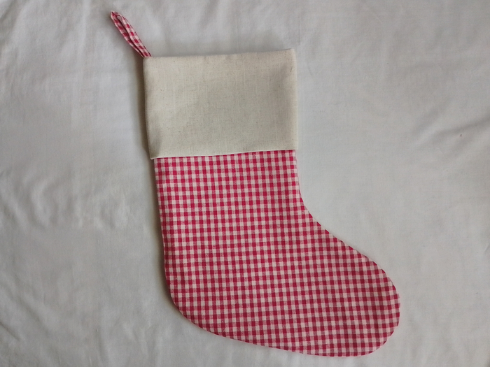 A finished Christmas stocking with a red and white gingham body and a solid off-white cuff, lying flat on a white background. A gingham hanging loop is visible at the top.