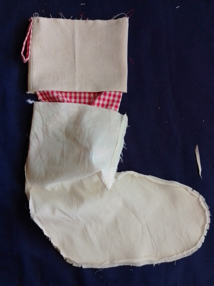 A red and white gingham stocking with its cuff attached, being inserted into an off-white calico lining stocking on a dark blue background.