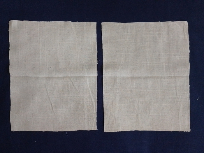 Two identical rectangles of off-white linen fabric with a crease in the middle lying side-by-side on a dark blue background.