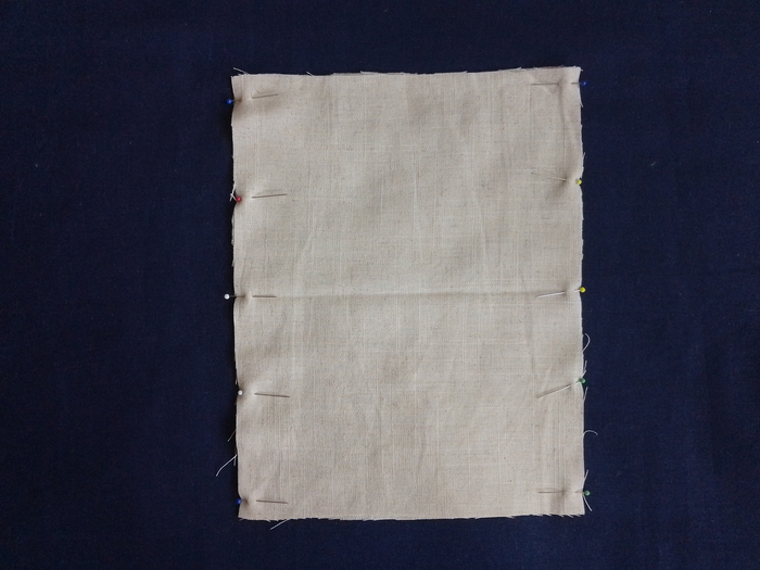 Two rectangles of off-white linen fabric on top of each other pinned together on the longer edges.