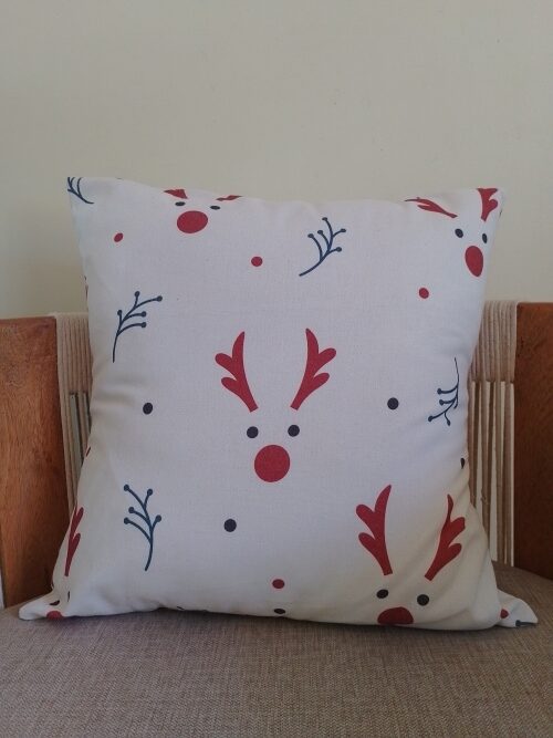 A finished envelope cushion sitting on a chair, seen from the front. The fabric is white with a pattern of red reindeer faces and green branches.