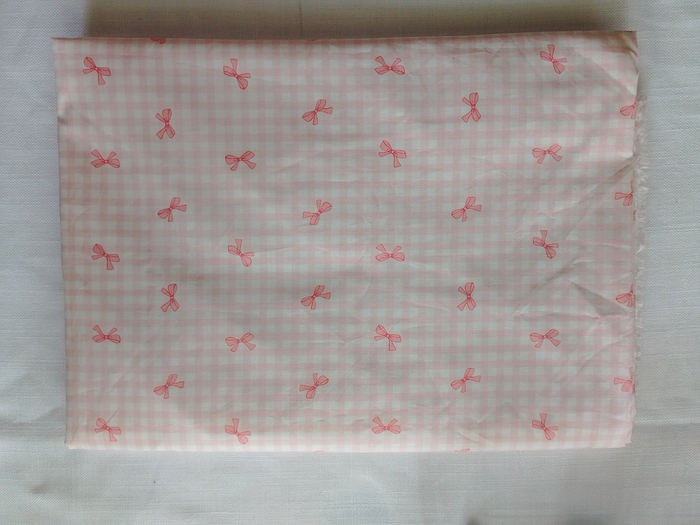 A folded piece of pink and white gingham fabric featuring a pattern of small pink bows.