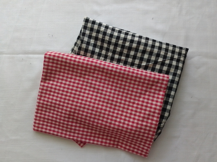 A folded piece of red and white gingham fabric stacked on top of a piece of black and white gingham fabric.