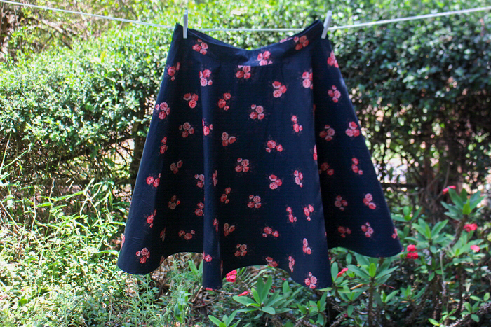 A navy blue three-quarter circle skirt with a pink floral pattern hanging on an outdoor clothesline.