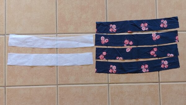 Four curved waistband pieces cut from floral fabric and two matching pieces of white interfacing, laid out on a tile floor.