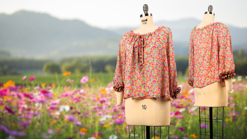 A dress form displaying a bright, multicolored floral print blouse with long sleeves, ruffled elastic cuffs, and a gathered neckline with a long center tie.