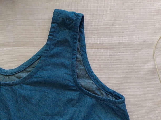 Close-up view of the shoulder and armscye of a blue chambray camisole, showing the seam finish and tight, unclipped armhole.