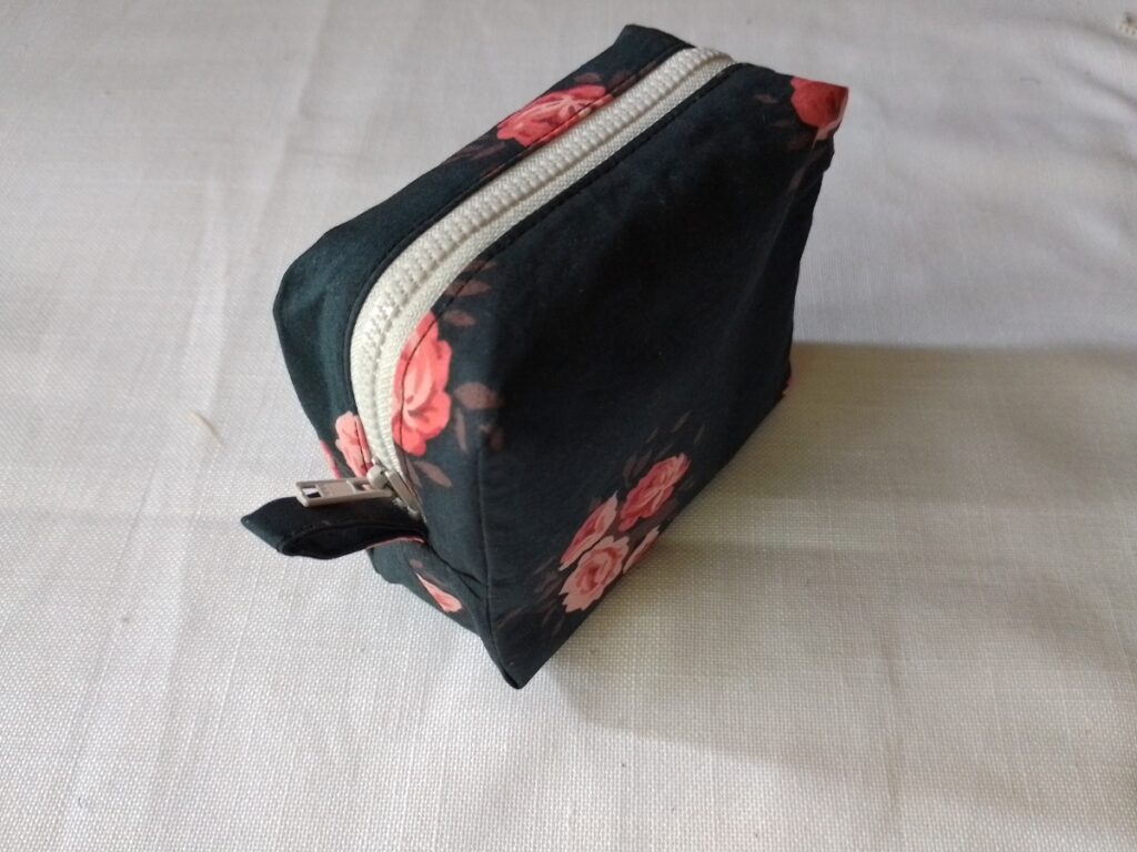 Top view of a square boxy pouch in dark floral fabric and an off-white zipper