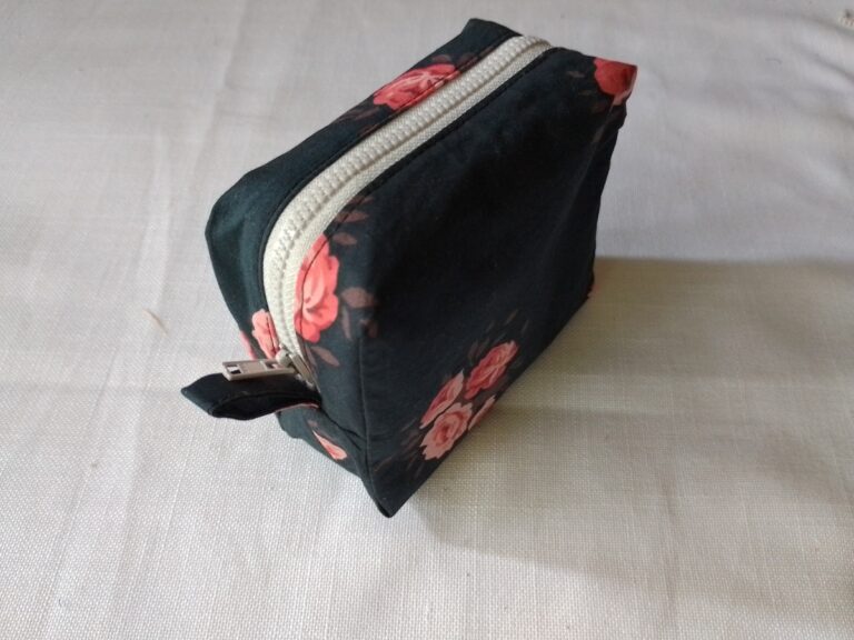 Top view of a square boxy pouch in dark floral fabric and an off-white zipper