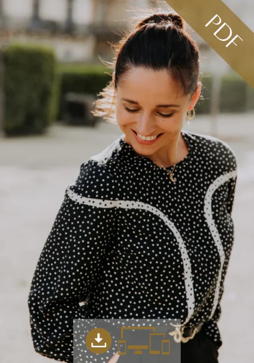 A woman smiling and looking down, wearing a black long-sleeved blouse with white polka dots and distinctive white curved piping details on the bodice and sleeves.