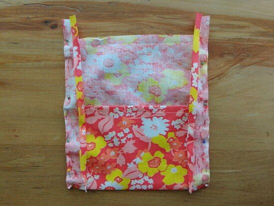 A small floral fabric pocket with open single fold binding pinned onto the side edges.