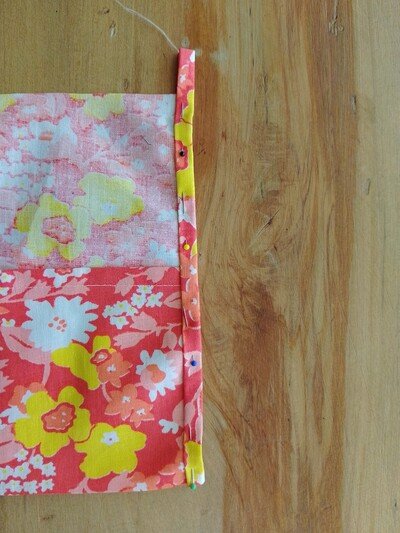 Floral fabric with a folded edge pinned in place on a wooden surface