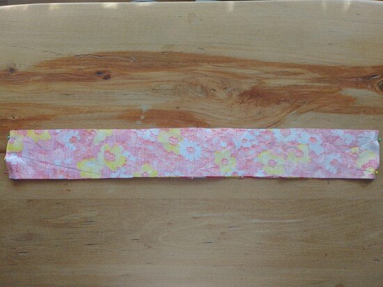 A long narrow strip of floral fabric pinned along both short edges on a wooden surface.