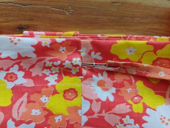 A close up of a tote bag with the casing secured with bar tacks. A bodkin attached to a drawstring is partially inserted into the casing of the tote bag