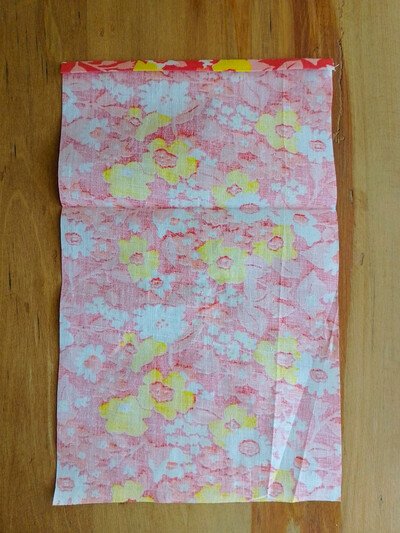 A rectangular piece of floral fabric folded at the top on a wooden surface.
