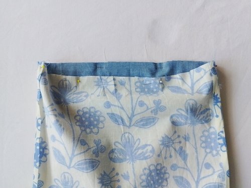 The top edges of the blue chambray lining and the floral main fabric aligned and held together with several sewing pins.
