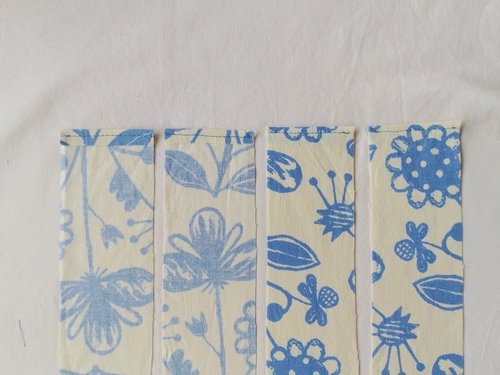 Four strips of of blue and off white fabric with a line of stitching at the top short edge