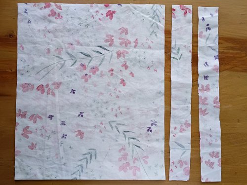 One large square piece of the floral fabric laid flat next to two long, thin cut strips of the same fabric.