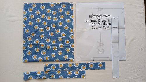 Blue daisy fabric pieces and paper sewing patterns laid out on a white surface.