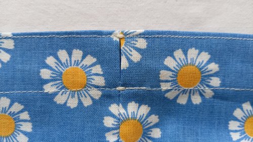 A close-up of a small opening in the fabric channel with white reinforcing stitches at the top and bottom.