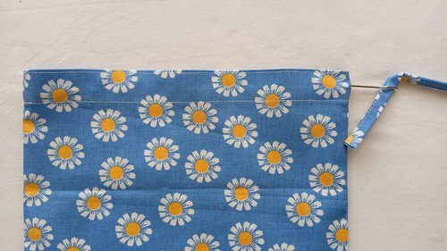 A metal tool pulling a blue fabric strap through a channel at the top of a blue floral bag.