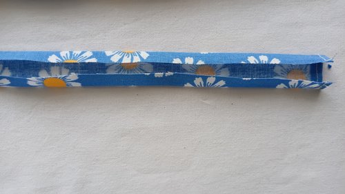A narrow strip of blue floral fabric with the long raw edges folded inward toward the center.