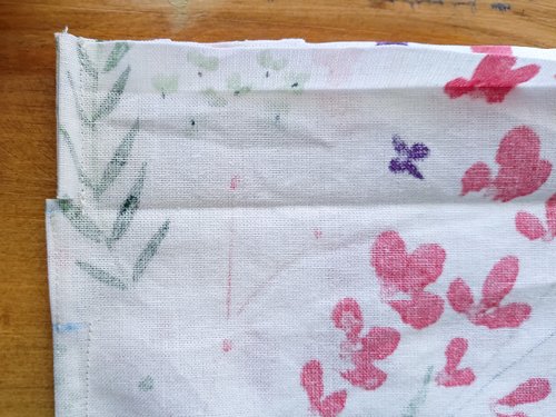 A close-up of the top corner of a sewn floral fabric with a snip at the bottom crease.