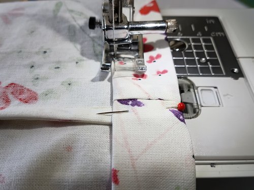 The top edge of a floral bag folded over, under the presser foot of a sewing machine